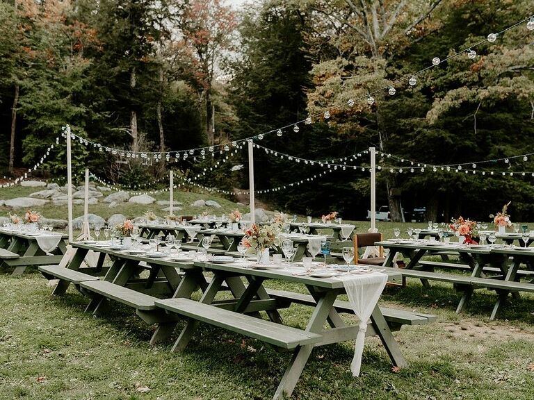 picnic tables at backyard wedding reception with bistro string lights on poles throughout the yard