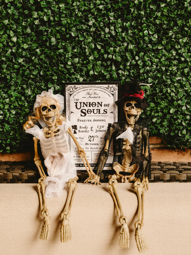 A spooky Halloween-inspired wedding welcome sign, complemented by a pair of skeletons dressed for the occasion.