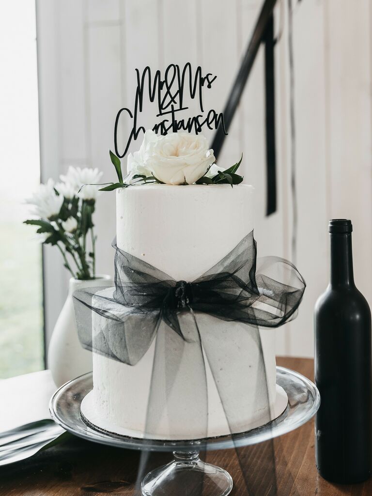 two tier white wedding cake decorated with black tulle bow, cake topper and white roses on top