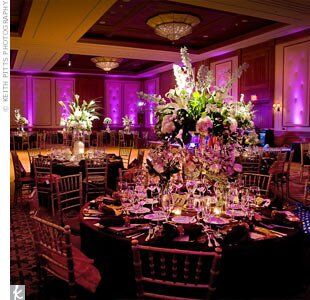 On the tables, a variety of white flowers, including calla lilies, lilies, roses, hydrangeas, delphiniums, and dendrobium orchids, picked up shades of magenta from the elegant lighting in the reception hall.