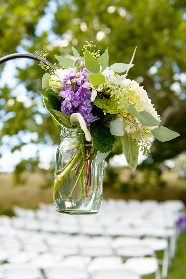 Mason jars hanging from shepherds' hooks while holding small bouquets of ivory and purple hydrangeas, calla lilies and roses lined the ceremony aisle.