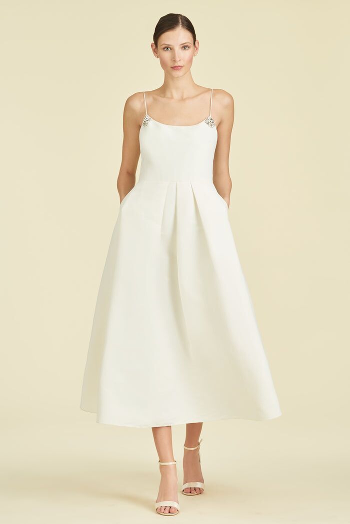 Model wears a fitted white dress with a fitted waist and full skirt. 