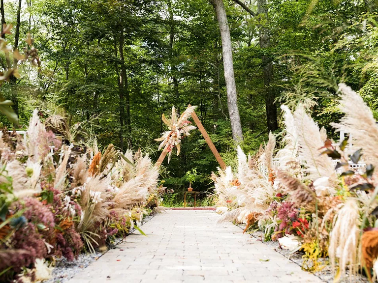 Pampas grass waves guests on towards a modern geometric wedding arch.