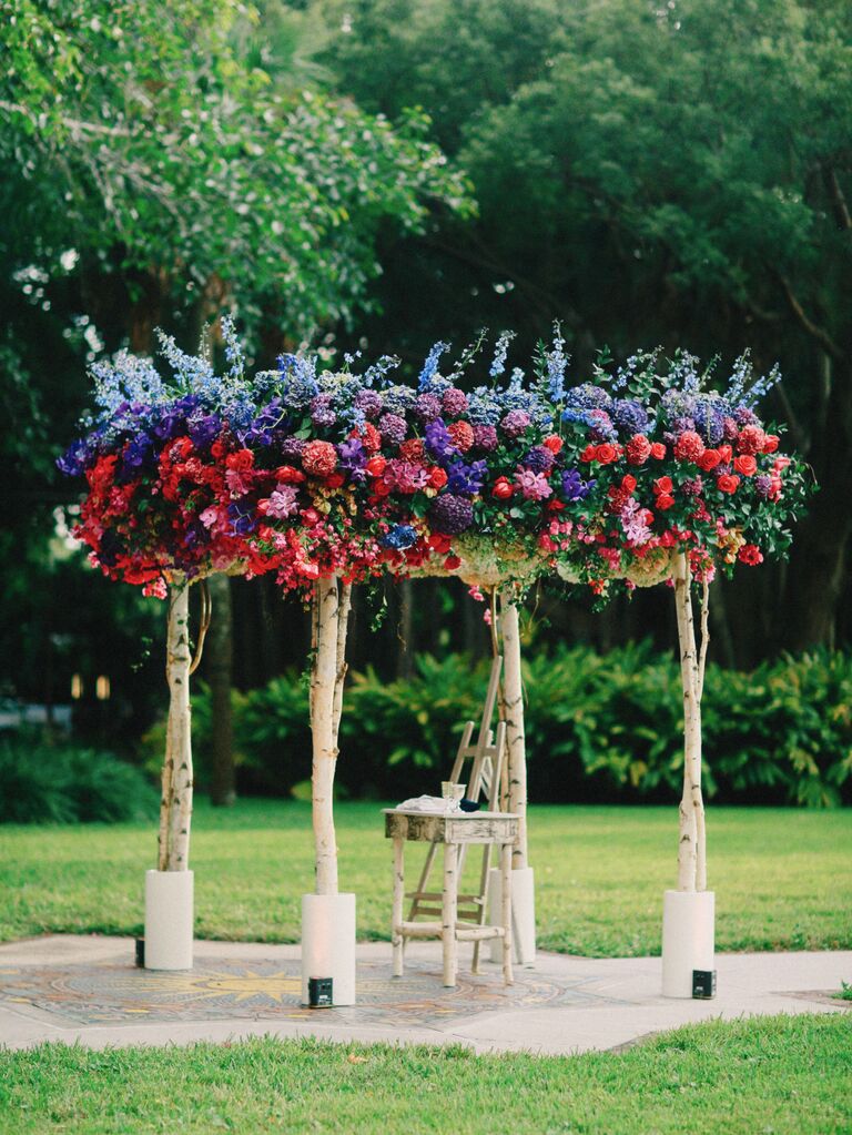 colorful wedding chuppah with blue delphinium, purple hydrangeas, red roses, pink orchids and greenery