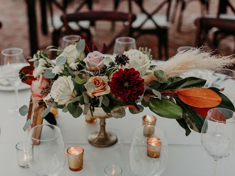moody boho low wedding centerpiece with white and pink roses, burgundy dahlias, magnolia leaves and pampas grass