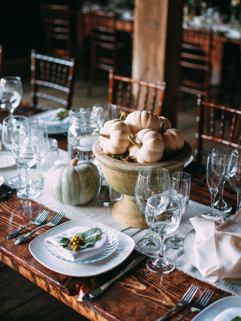 rustic fall wedding centerpiece with mini white pumpkins in stone urn vase on bare wooden table