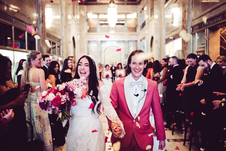 Brides Walking Up Aisle While Guests Throw Rose Petals, Pink Flowers and Suit