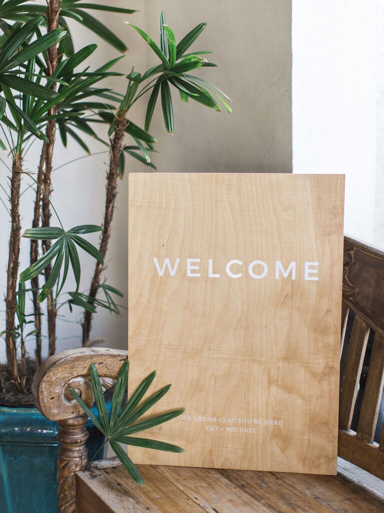 simple wedding welcome sign with modern white typeface on plain wooden board