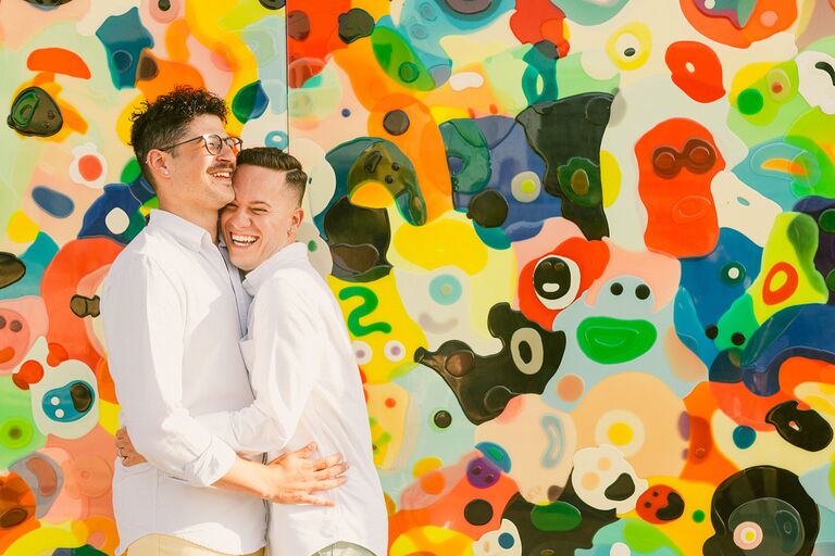 Grooms hugging in front of colorful mural