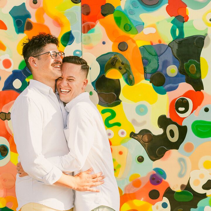 Grooms hugging in front of colorful mural