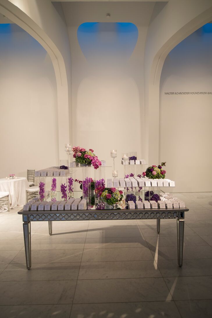 The escort card table mirrored the look of the rest of the wedding. Black-and-white cards with formal script sat atop Lucite display boxes on a metallic table. Vibrant pink and purple flowers and tea candles enhanced the display.