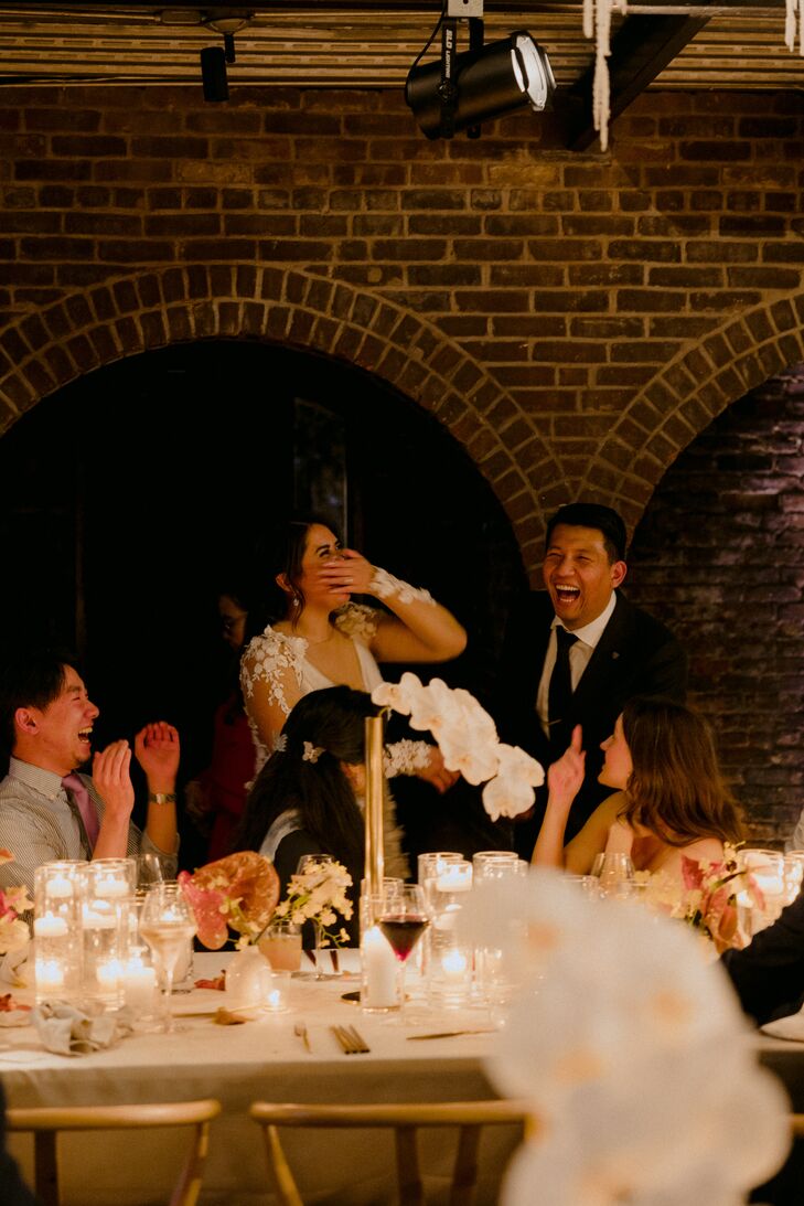 Bride and Groom Laughing, Standing Behind Guests at Long Reception Table, Candles and Orchids