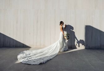 Bride shows off a beautiful white lace gown in front of a gray wall. 
