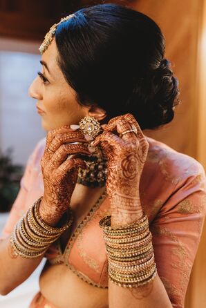 Bride With Henna, Bangles Putting on Ornate Gold Earrings for Indian-American Wedding