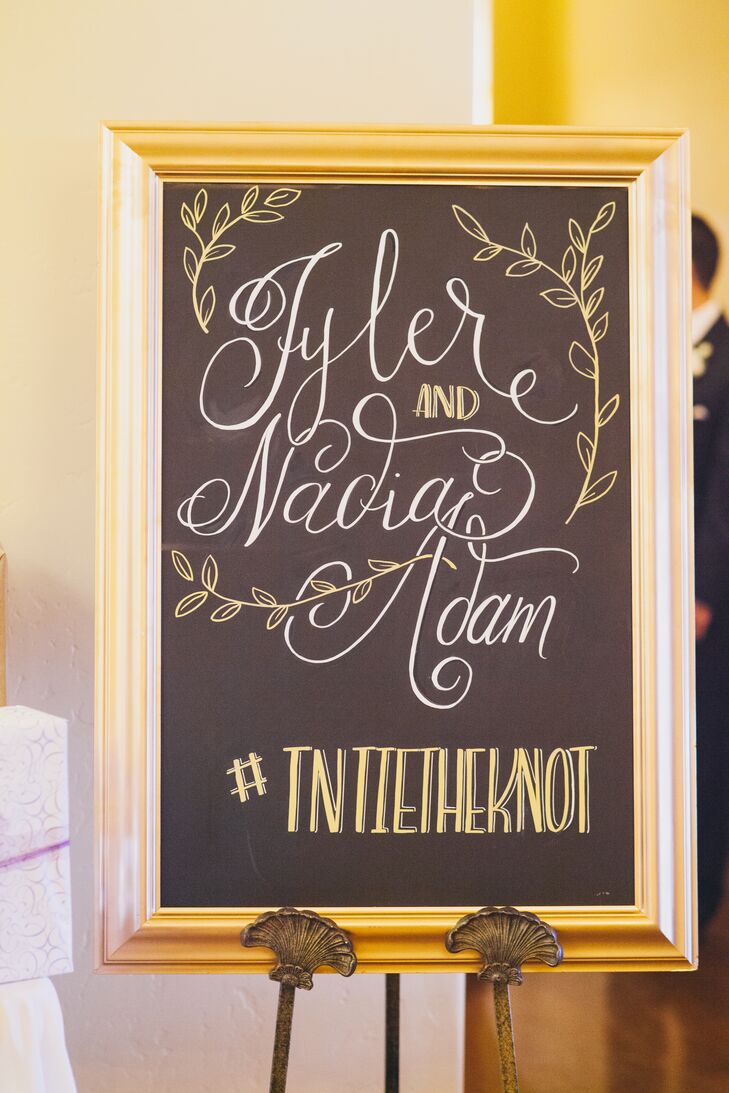 A gold glamorous frame bordered a black chalkboard sign that read "Tyler and Nadia Adam" with sketches of leaves surrounding the text. Their hashtag, written at the bottom, encouraged guests show off the wedding over social media throughout the day.