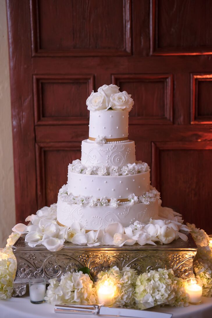 Creative Cake Factory baked a classic all-white confection for Melissa and Derek that was composed of red velvet and chocolate cakes. A slight champagne ribbon along each base was met with white delphinium blooms and swirl or dotted piping. White roses served as the topper. “I cannot wait to eat it on our one-year anniversary,” Melissa says.