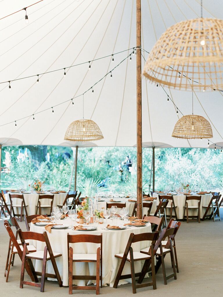 Neutral rattan chandeliers hanging from white outdoor wedding tent
