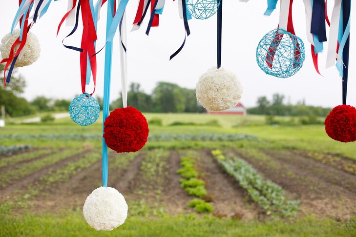 Red and white carnation pomanders and spheres made of blue string hanging from matching ribbons hung on the ceremony arch.