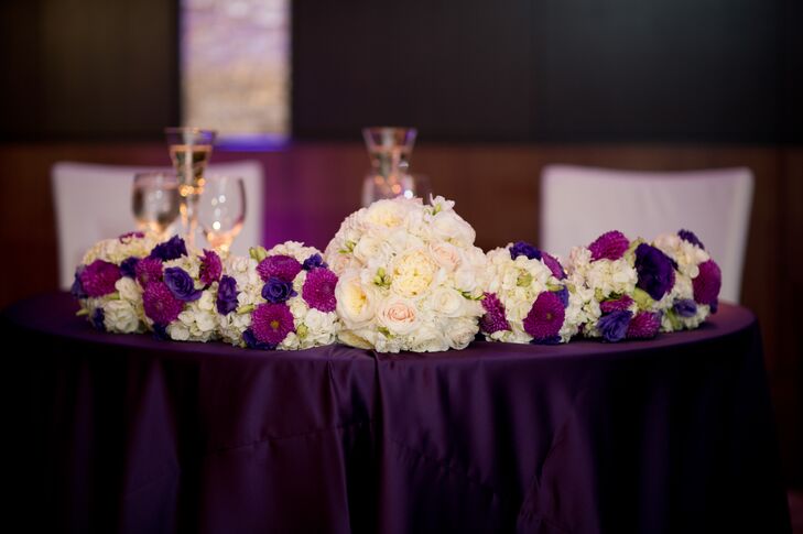 The bride and groom's circular sweetheart table was covered in sumptuous royal purple linens and eye-catching white and purple florals in small and large arrangements.