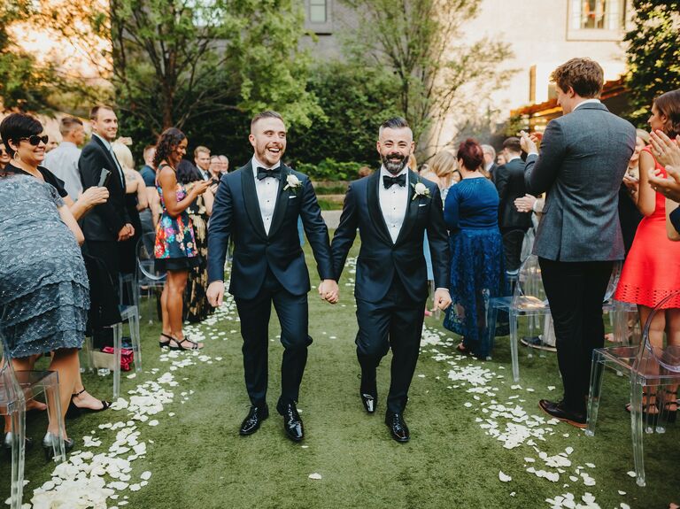 Grooms walk down the aisle wearing tuxedos. 