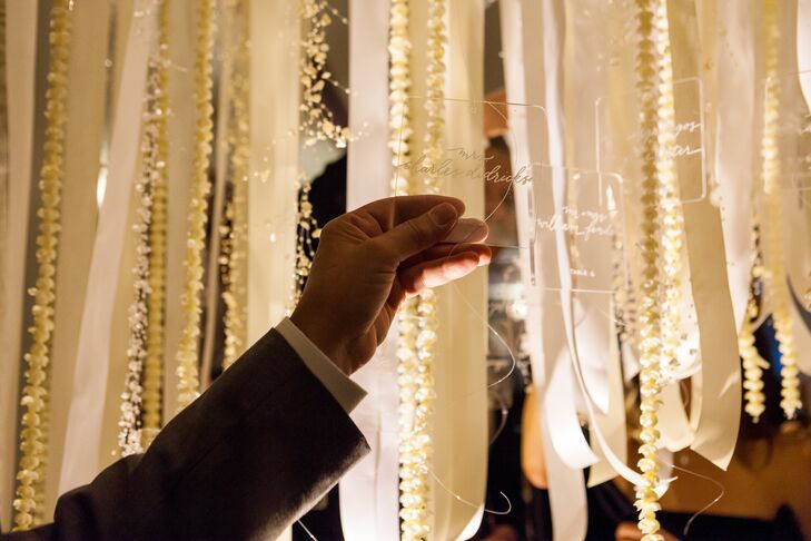 A unique alternative to a traditional escort card display, guests found their names and table assignments calligraphed on 120 acrylic escort cards hanging from the ceiling on white satin ribbons. The display was made into an arch so guests could walk underneath it and cut down their names. Bonus: they could take their cards home to use as a paper weight!