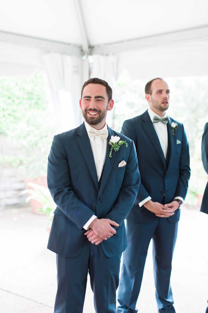 “Eric has awesome blue eyes that look amazing when he wears blue,” Brianna says. It was no surprise that he waited for her at the altar in a slate blue tuxedo. His accessories only highlighted the look. Eric wore a white shirt, ivory bow tie, matching pocket square and this sweet white freesia boutonniere with a succulent.