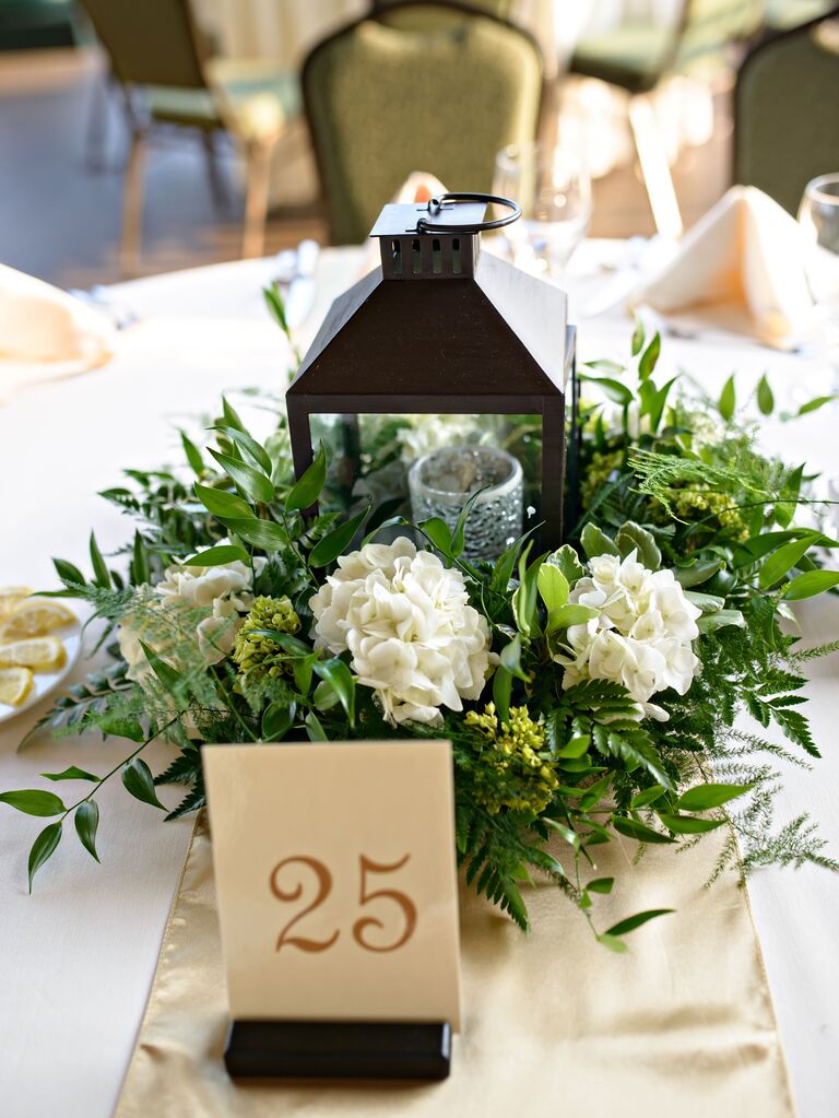 wedding centerpiece with bronze hurricane lantern, white hydrangeas and fresh smilax vines