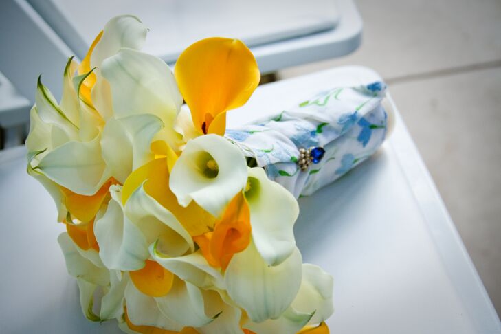 The bridal bouquet was a canary yellow and ivory assortment of calla lilies. A white wrap adorned with a blue floral design wrapped around the stems of the bouquet and was clipped with a sapphire stone.