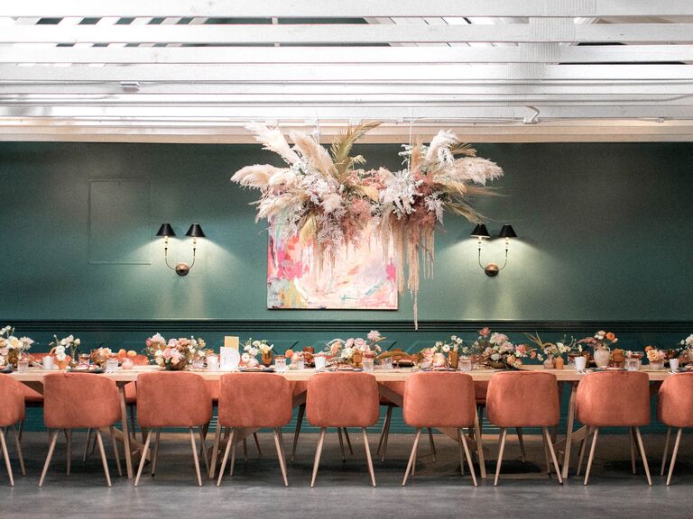 restaurant wedding venue with hanging pampas grass installation above long banquet table with orange velvet chairs