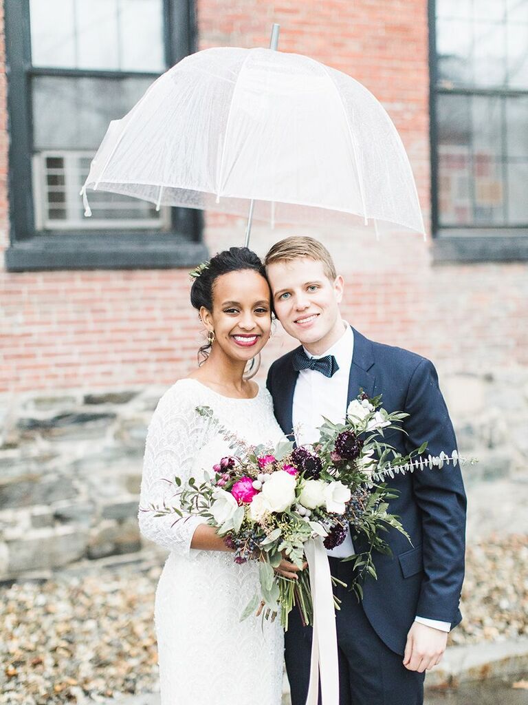 bride and groom under umbrella holding wild bouquet