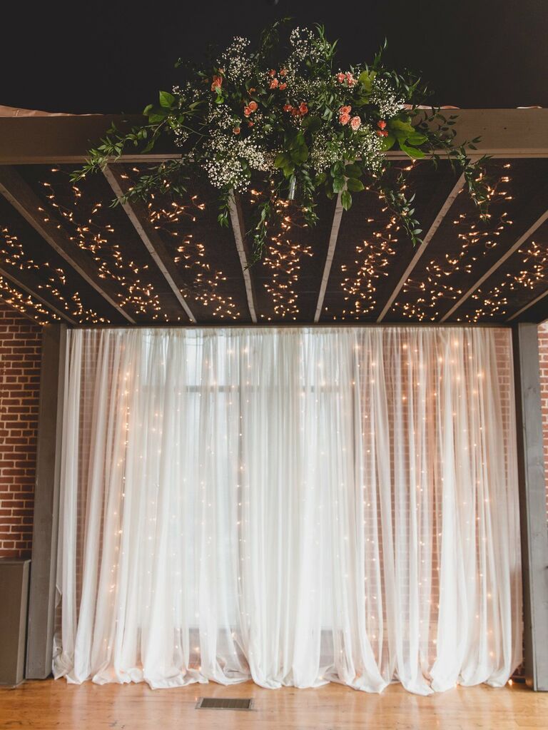 wedding ceremony backdrop with string lights showing through sheer white curtain 