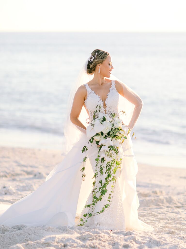 bride standing on the beach holding oversized cascading wedding bouquet with white flowers and vines touching the ground