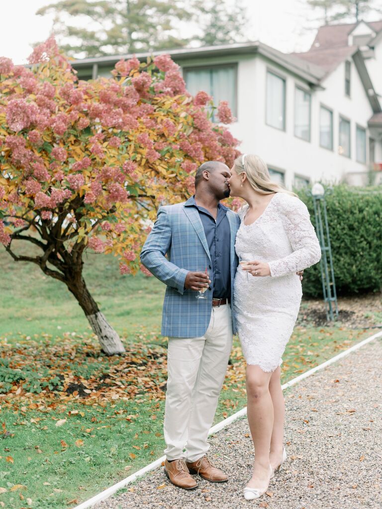 A couple share a kiss outside beside an autumnal tree