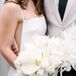 A bride in a modern gown with deep-v side panels holding an all-white bouquet of calla lilies, roses and more, some cascading down.