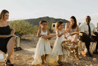 Toddler flower girls in white dresses walking down aisle at outdoor wedding
