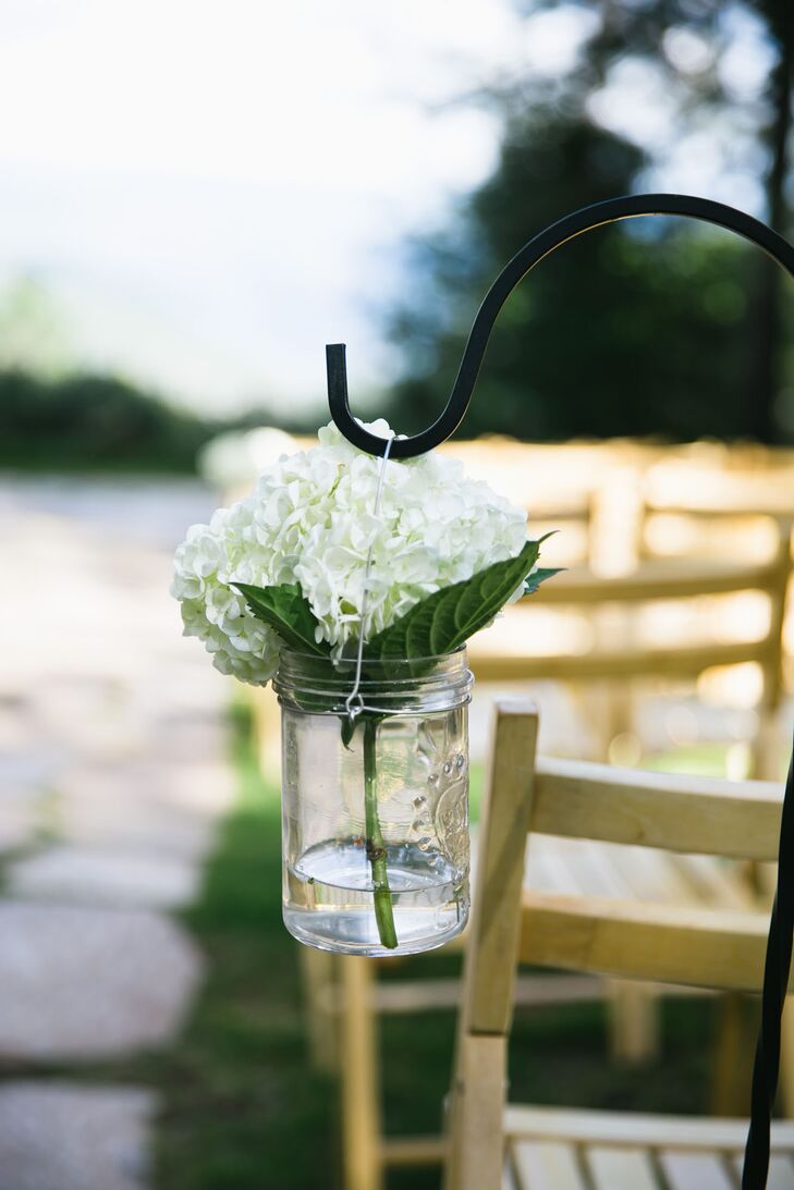 White hydrangeas were arranged in glass jars and hung from metal hooks, lining the ceremonial aisle outside at Forest House Lodge in Foresthill, California. Little to no decor was added to the outdoor ceremony space, which brought focus to the natural elements.