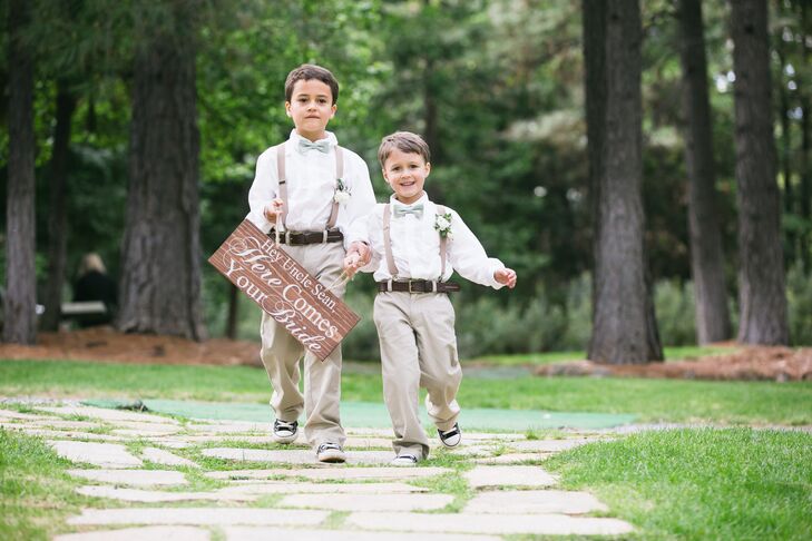 The ring bearers walked down the aisle wearing matching khaki pants with brown suspenders, and a white button-up shirt complemented by a green bow tie. They each wore an ivory rose boutonniere pinned to their suspender strap and held a wooden wedding sign that read "Hey, Uncle Sean, Here Comes Your Bride."