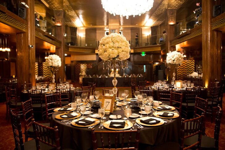 Reception dining tables were set with black linens and gold dinnerware, surrounding the tall centerpieces filled with ivory roses and hydrangeas created by Lavenders Flowers.