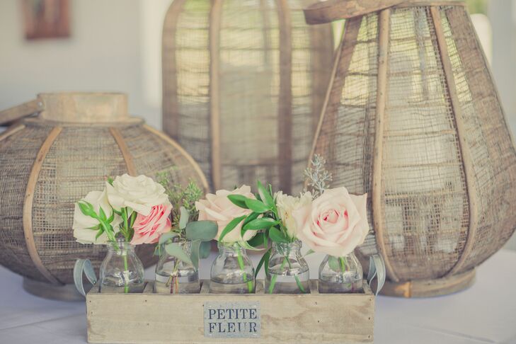Pink and ivory roses were arranged in glass vases and placed inside a rustic wooden box. Behind the box were tall lanterns made of branches with candles inside.