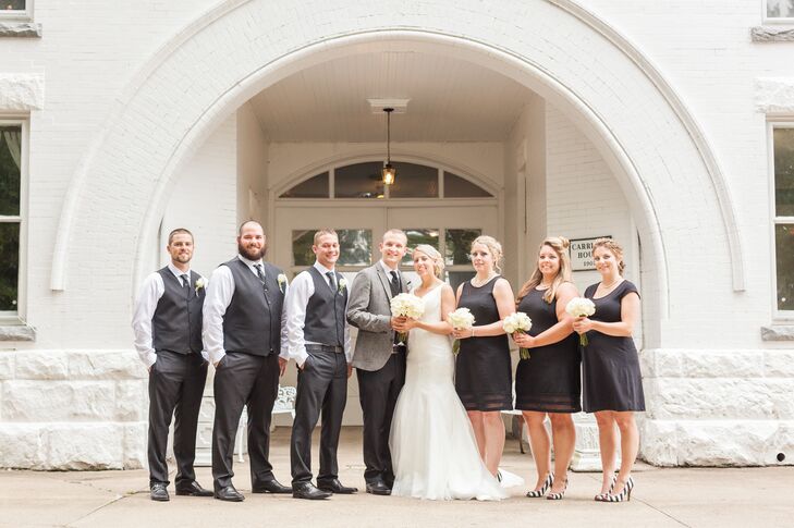 Anna and Tyler stood in the middle of their wedding party dressed in black-and-white attire, following the color palette of the wedding day. The groomsmen wore charcoal gray vests and pants and the bridesmaids wore black knee-length cocktail dresses.