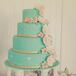 The intricate blue four-tiered wedding cake was designed with cake flowers and gold ribbon at the base of each tier. The cake stand was designed to look like white pillars with a mini fountain in the middle, surrounded by flowers.