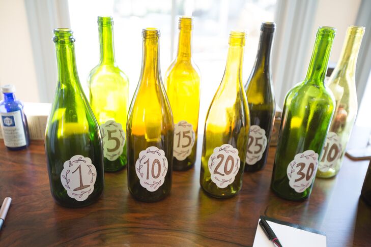 The table numbers for Brittany and Seth's wedding were displayed on green wine bottles. On each table, there were pictures of the couple at the age of the corresponding table number.
