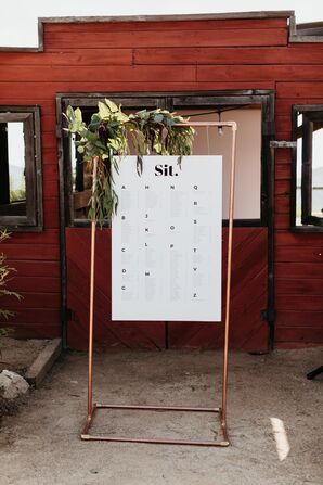 Rustic Seating Chart with Greenery Hanging from Copper Pipe Easel