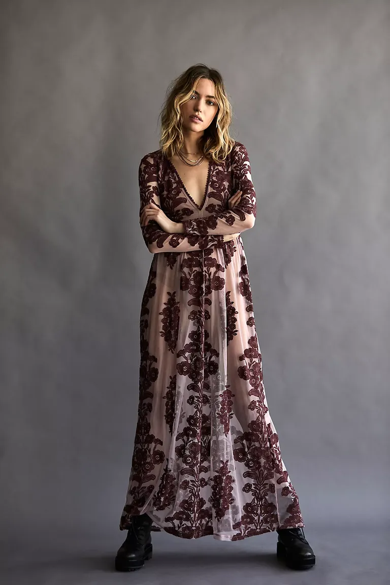 Model wears a long sleeved dress with floral detailing and a sheer finish. 
