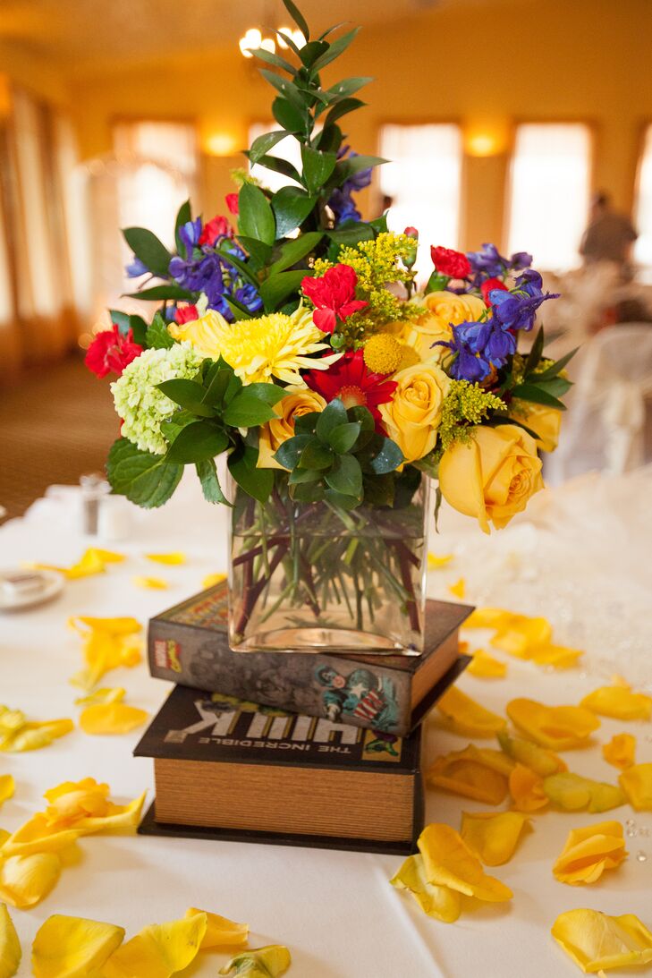 Colorful centerpieces of roses, hydrangeas and other flowers were arranged in a glass vase. The centerpiece was positioned on top of books surrounded by yellow rose petals. “For the centerpieces, we wanted live flowers and chose white hydrangeas arranged in a comic book decoupage box,” says Rebecca.