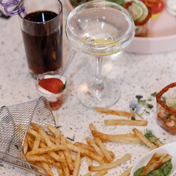 A fancy cocktail glass with small bites and french fries strewn across a counter-top.