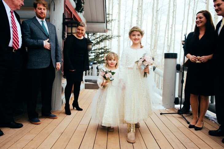 The flower girls wore sparkly gold dresses with a light tulle overlay on the skirt. They completed their look with rosette-patterned white sweaters since the winter wedding was outside. They carried small rose and lamb’s ear bouquets and wore flower crowns that matched the bride.