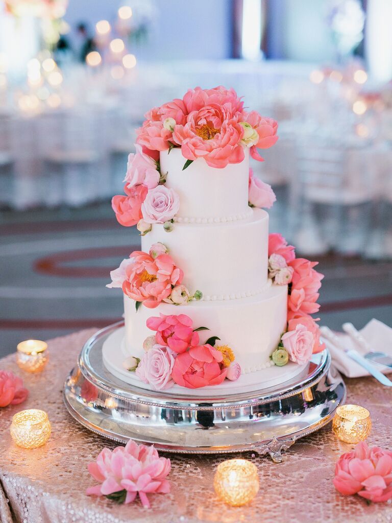 three tier white wedding cake on silver round base with lilac roses and coral peonies