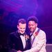 Grooms in Black-and-White Tuxedo Jackets Cutting Cake Under Purple Lighting