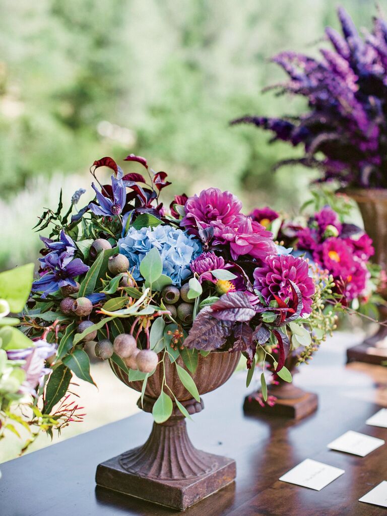 small wedding centerpiece with magenta, purple and blue flowers in stone urn vase